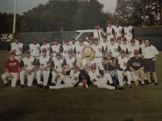 The 2001 Tyler Roughnecks team photo: players in white pinstriped uniforms and red caps posed in rows on the field with the team's fuzzy orange mascot